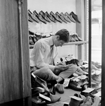 126839 Afbeelding van een schoenverkoper tijdens het afprijzen de collectie in verband met uitverkoop in een ...
